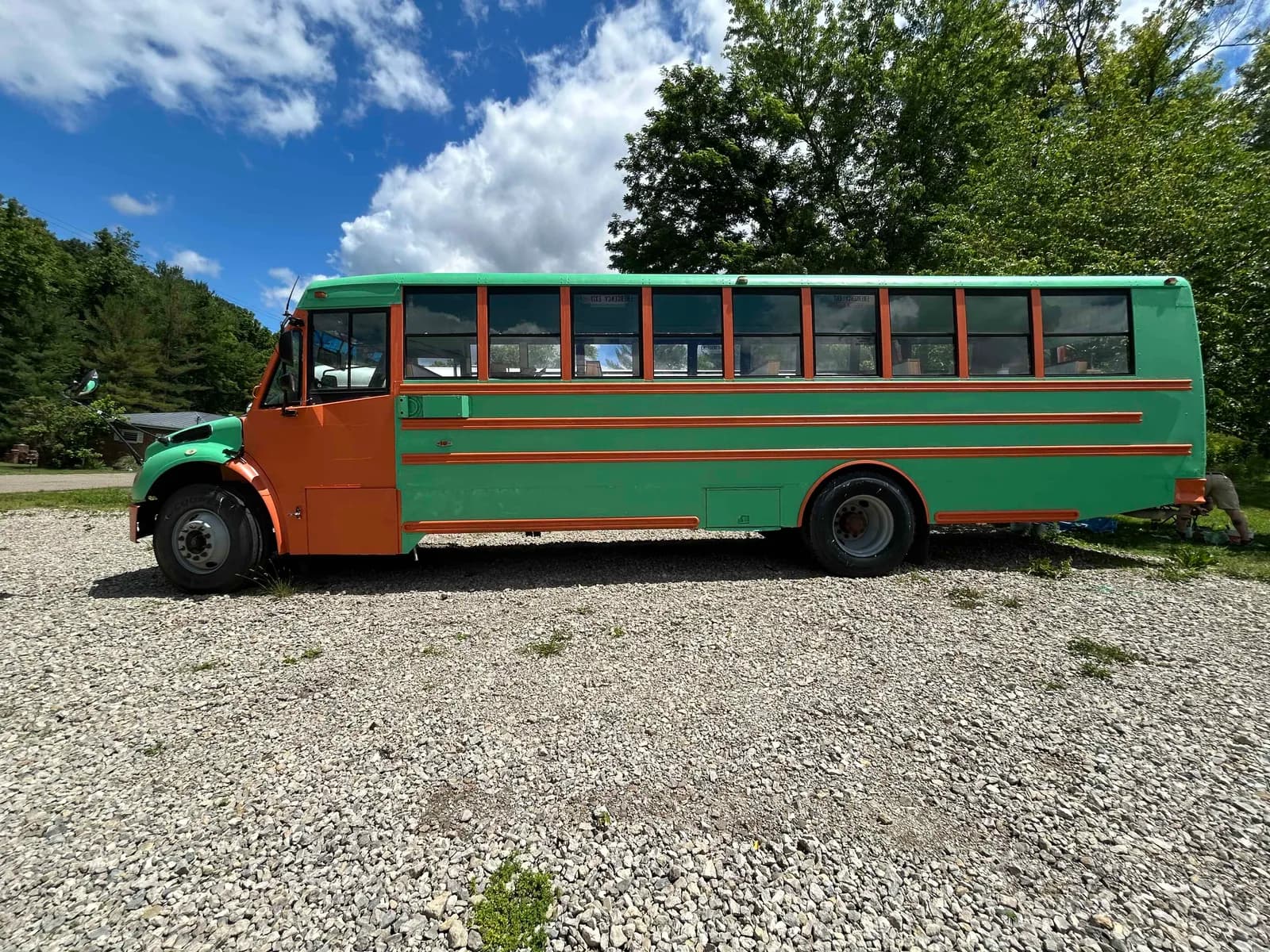 Full side profile of the green-and-orange Rolly Tour Bus on the gravel lot