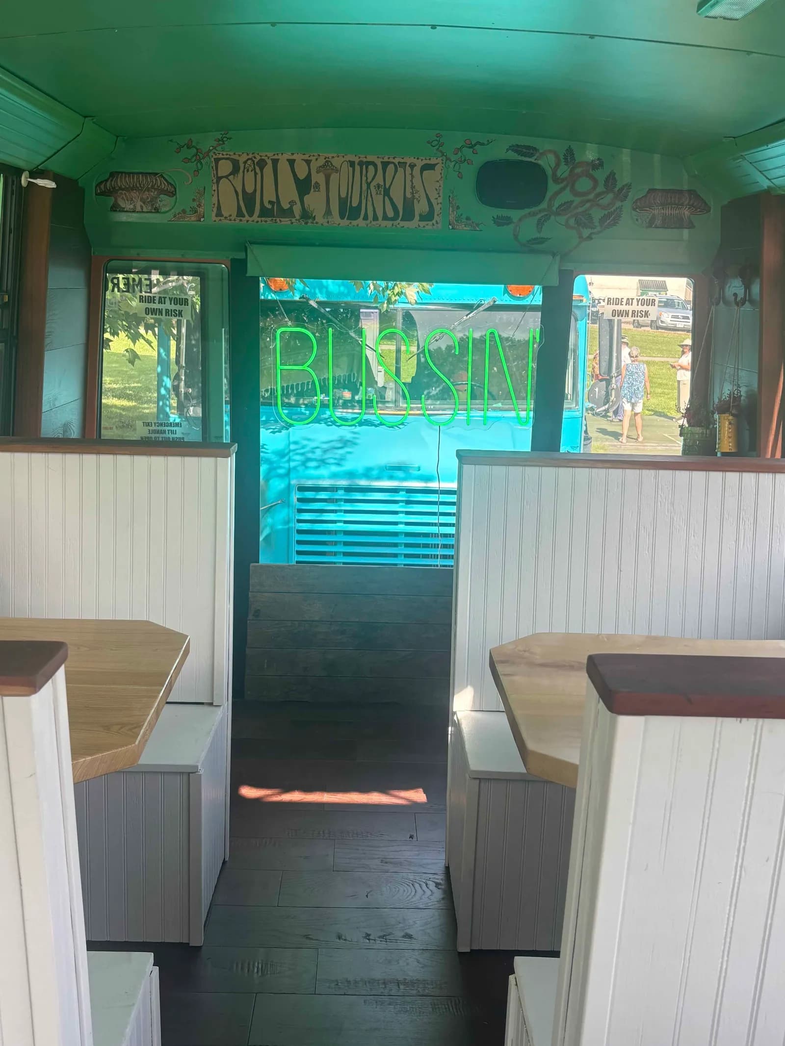 Hand-painted 'Rolly Tour Bus' sign and a green 'Bussin' neon inside the bus