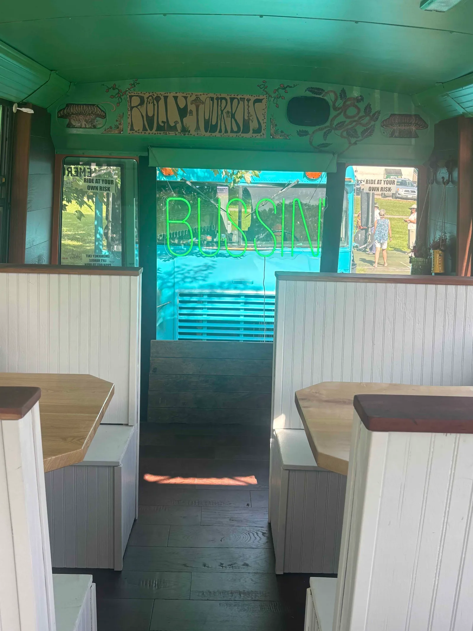Hand-painted 'Rolly Tour Bus' sign and a green 'Bussin' neon inside the bus